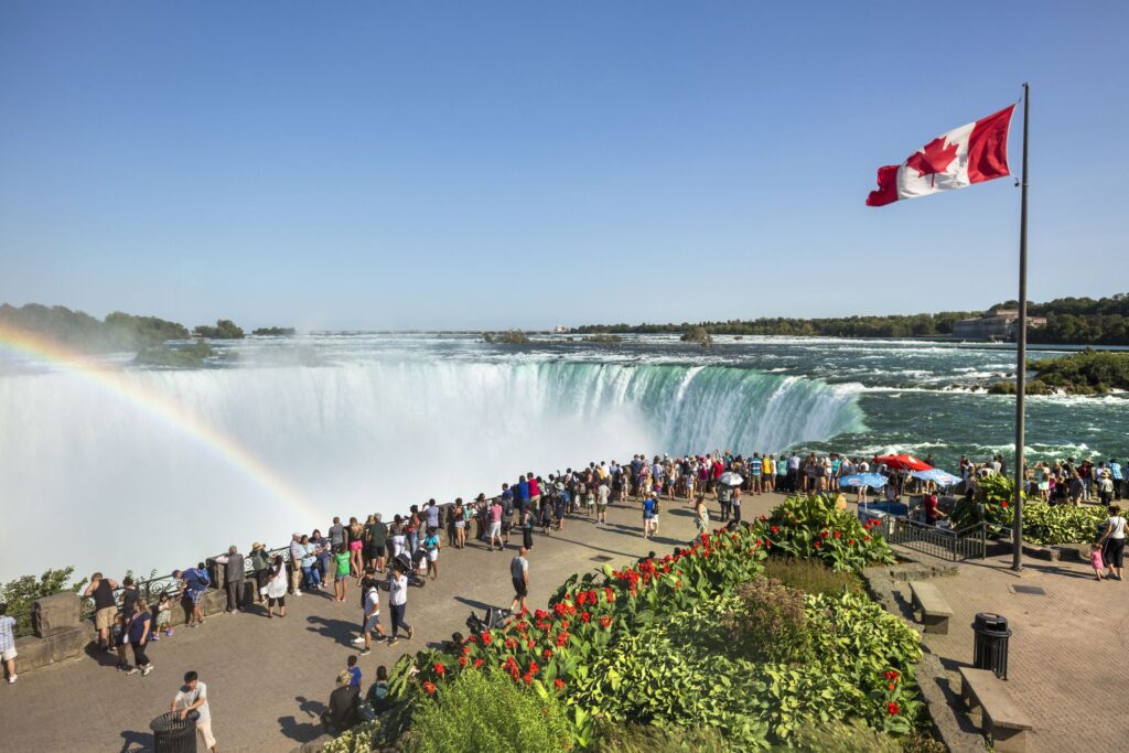 crowd of people next to waterfall and canadian flag on pole