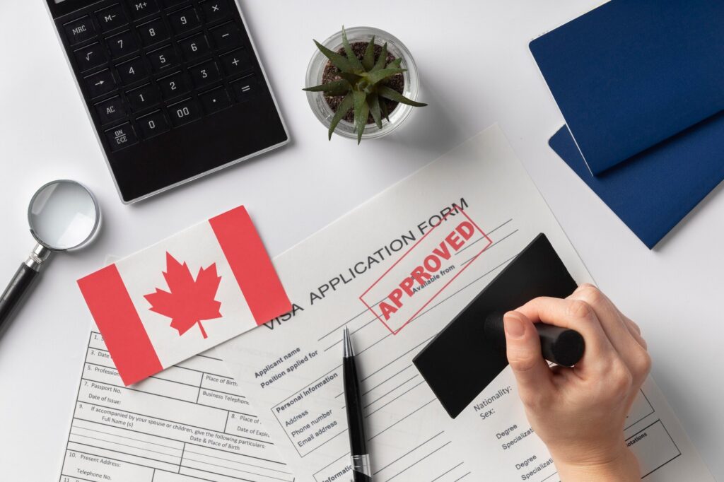 hand holding stamp over visa application form next to canadian flag